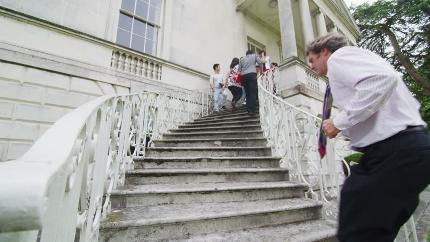 Diverse group of students and teachers using the staircase outside an elegant historic university building.