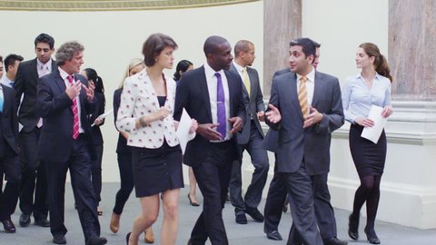Diverse group of confident and successful business delegates, chatting together as they walk through an elegant, classically designed conference building. In slow motion.