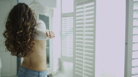 4k / Ultra HD version Beautiful young woman getting dressed in her elegant apartment. Sunlight streams in as she goes to the window to take a look at the view outside. In slow motion. Shot on RED Epic