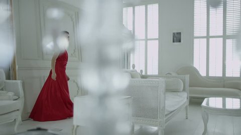 4k / Ultra HD version Happy and beautiful brunette in red evening gown runs to look out of the window in her elegant white apartment. In slow motion. Shot on RED Epic