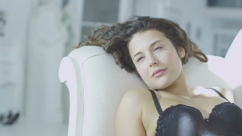 4k / Ultra HD version Beautiful brunette model in black lingerie reclines on a chaise and relaxes in the sunlight from the window. Shot on RED Epic