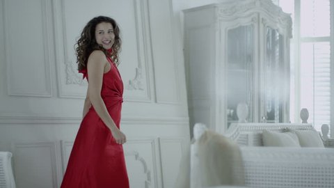 4k / Ultra HD version Happy and beautiful brunette in red evening gown runs to look out of the window in her elegant white apartment. In slow motion. Shot on RED Epic