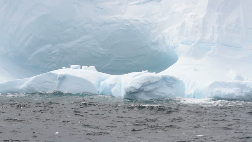 Close up of arches in large tabular iceberg in rough seas of Drake Passage near Antarctica on stormy day.

