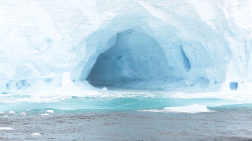 Close up of arches in large tabular iceberg in rough seas of Drake Passage near Antarctica on stormy day.
