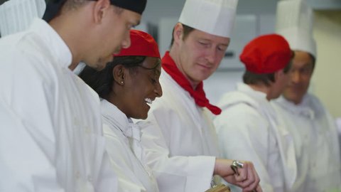 4k / Ultra HD version Mixed ethnicity team of professional chefs preparing and cooking food in a commercial kitchen. The head chef tastes a dish and gives her approval. In slow motion Shot on RED Epic