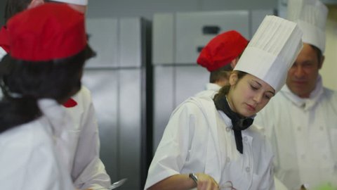 4k / Ultra HD version Mixed ethnicity team of professional chefs preparing and cooking food in a commercial kitchen. The head chef tastes a dish and gives his approval. Shot on RED Epic