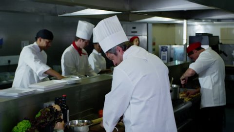 4k / Ultra HD version Portrait of a smiling head chef in a commercial kitchen with his team of staff working in the background. In slow motion. Shot on RED Epic