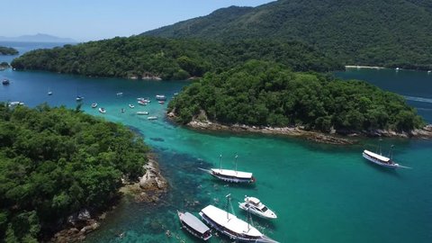 A aerial drone shot revealing a bay full of tourist schooners and boats on a paradisiac and hidden Caribbean style wonderful island of clear and transparent water with jungle, rocks corals and reefs.