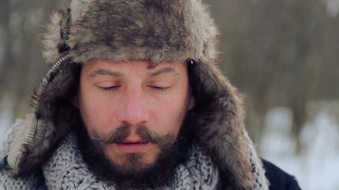 Portrait of a bearded man with an apple in the winter. A young bearded man eats an apple in the winter. The bearded man eating an apple to the camera in the winter. 