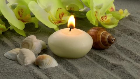 Candle and seashells on the sand with orchid flower