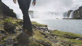 Couple visiting majestic Godafoss waterfall. Man and woman are on vacation at beautiful waterfall in Iceland. Male and female tourists are walking at famous attraction.