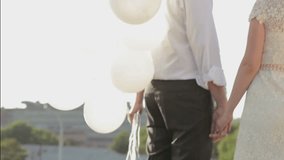 Happily married couple holding hands and white balloons. 