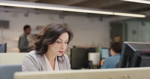 Businesswoman executive working at computer using smart phone connected to global data in busy corporate office
