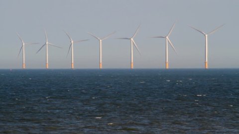 A small boat passes in front of the turbines of an offshore wind farm