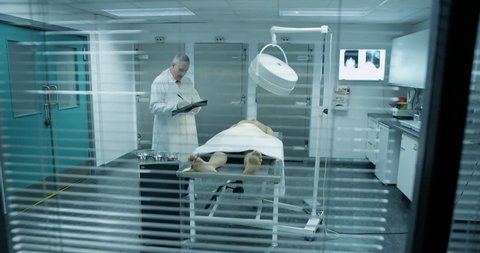 4k / Ultra HD version The lifeless naked corpse of a young mixed race male is laid out on the autopsy table, ready for the medical examiner. He checks the toe tag and starts to make notes.