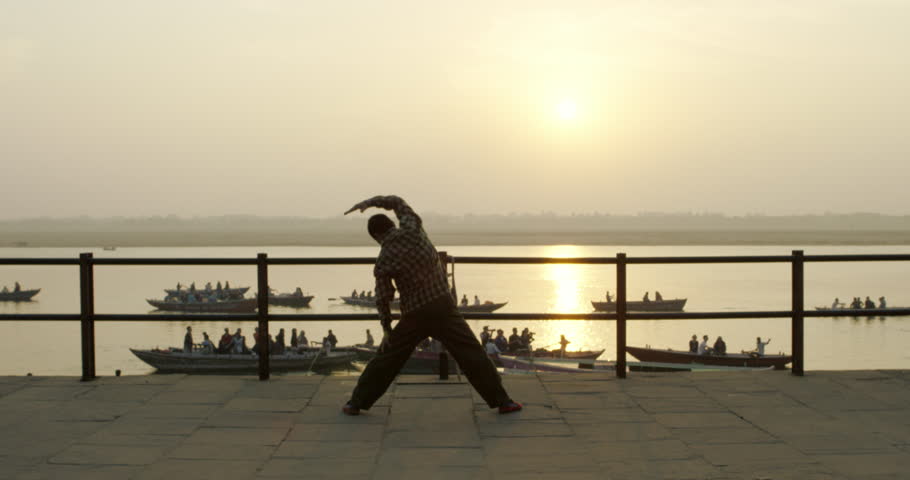 India, Varanasi - Man stretching overlooking Ganges river with boats passing underneath him. The sun is rising sunrise gold light golden hour silhouette of man stretching at a gath | Shutterstock HD Video #14150072