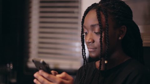 Black girl shocked and surprised at what she sees on her cell phone smartphone in the kitchen