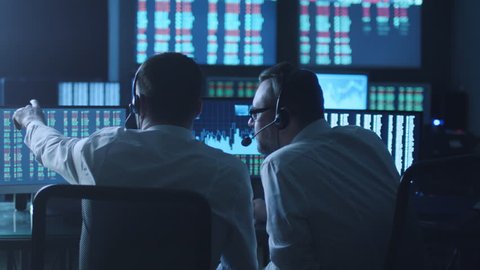 Team of stockbrokers are having a discussion in a dark office with display screens. Shot on RED Cinema Camera in 4K (UHD).