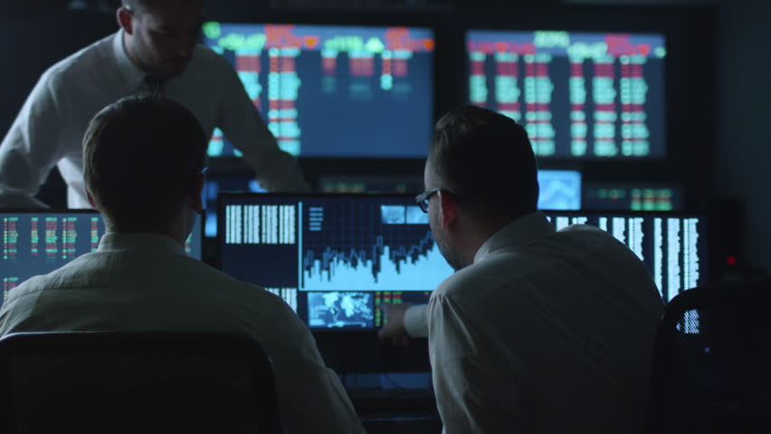 Team of stockbrokers are having a conversation in a dark office with display screens. Shot on RED Cinema Camera in 4K (UHD). Royalty-Free Stock Footage #14161592