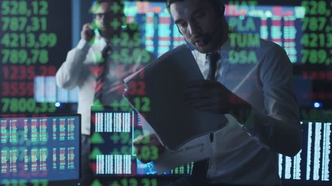 Stockbroker in white shirt is talking on the phone while working in a dark monitoring room with display screens. Shot on RED Cinema Camera in 4K (UHD).
