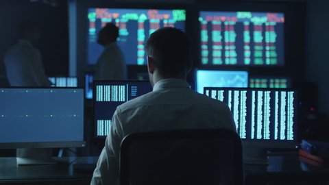 Stockbroker spotted a positive trend in trading charts while working in a dark monitoring room with display screens. Shot on RED Cinema Camera in 4K (UHD).