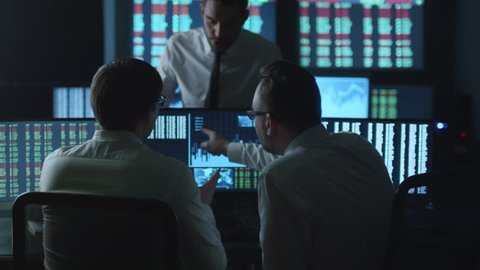 Team of stockbrokers are having a conversation in a dark office with display screens. Shot on RED Cinema Camera in 4K (UHD).