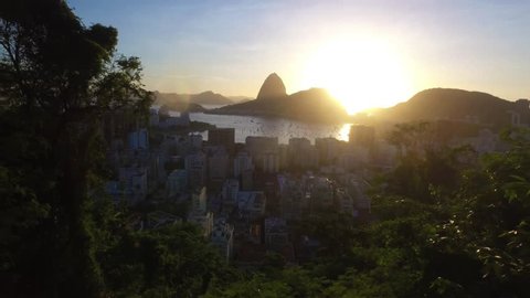 Avião de linha aérea comercial entrando no enquadramento para aterrissar na cidade maravilhosa do Rio de janeiro, ao fundo sol nascendo no cartão postal Carioca, o Pão de Açucar na Baia de botafogo. 