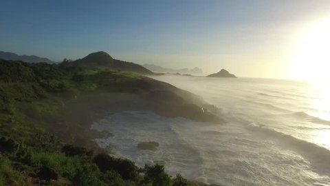 Drone view of a mythical scenery in a bucolic coast during sunset on a romantic morning in Rio de Janeiro. A classic road beside a calm sea with some beautiful waves ins a surf & sports paradise city 