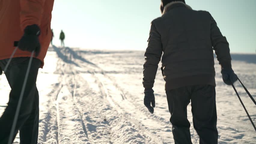 4k footage, back view two senior men pulling their toboggans up snowy hill on sunshine winter day, their wifes waiting on top
