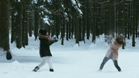 120 FPS Slow motion of two cheerful young adult attractive Caucasian girls having a snowball fight in winter forest. Shot with Blackmagic URSA Mini.