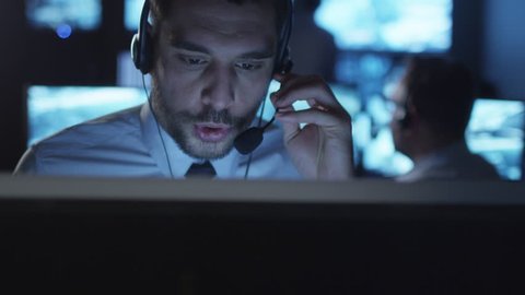 Happy technical support specialist is drinking coffee while working on a computer in a dark monitoring room filled with display screens. Shot on RED Cinema Camera in 4K (UHD).