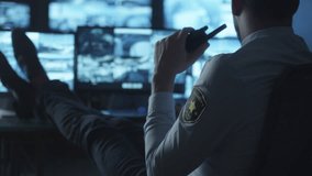 Security officer is relaxing at a computer desk while drinking coffee in a dark monitoring room filled with display screens. Shot on RED Cinema Camera in 4K (UHD).