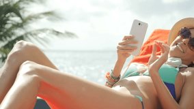Cheerful funny girl relaxing in long chair with smartphone