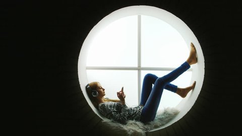 Attractive woman sitting at the round window, listening to music. - Βίντεο στοκ