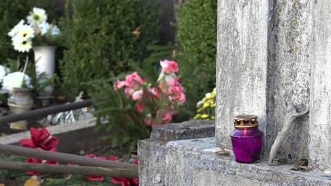 old grave with burning purple candle and flowers and candles in day of all dead. Small crucified jesus. Static closeup shot. 4K
