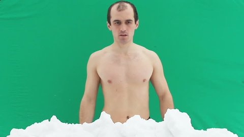 Young man with naked torso doing bumps in the snow on a green background