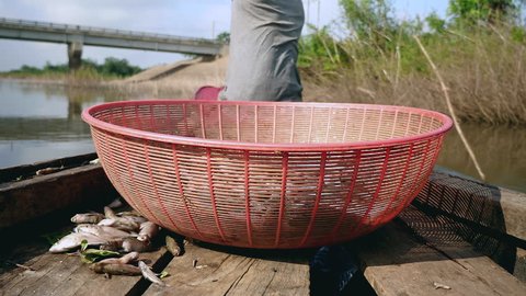 Close-up on a plastic fishing basket in a dugout canoe; Fisherman sitting in the bow rowing the boat on a lake