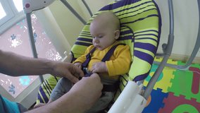 Father man put newborn baby boy or girl in special colorful swing and clip safety belt at home. Infant child sleep time. Camera mounted on swing. Wide angle shot. 4K UHD video.