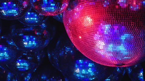 Mirror balls reflect rays of colored lights. Colorful reflective disco mirror ball with glinting highlights spinning slowly on a blurry colored background in disco club. The light show at night.