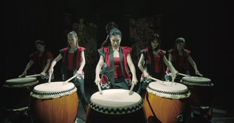 a group of Japanese Taiko drummers girls , start playing with the jump dark background, slow motion