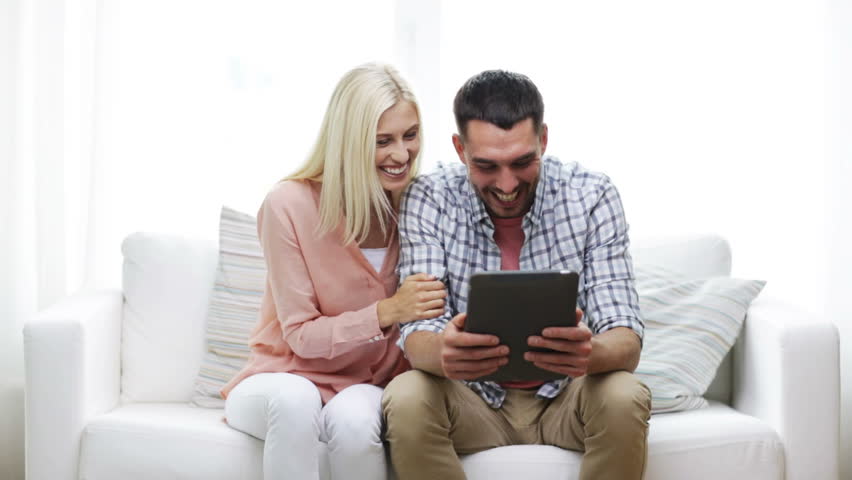 happy couple with tablet pc viewing photos at home