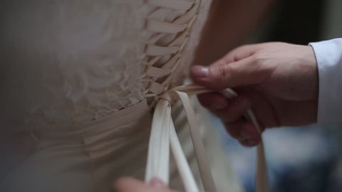 Man tying a corset on the bride's wedding dress.