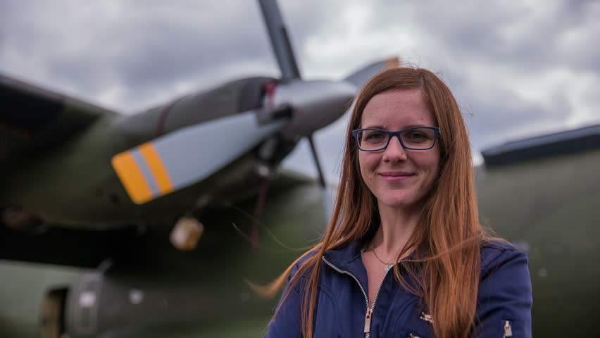 Woman portrait in front of an old aircraft. Young beautiful woman with stylish army jacket stand in front of older bomber aircraft with a propeller in background.