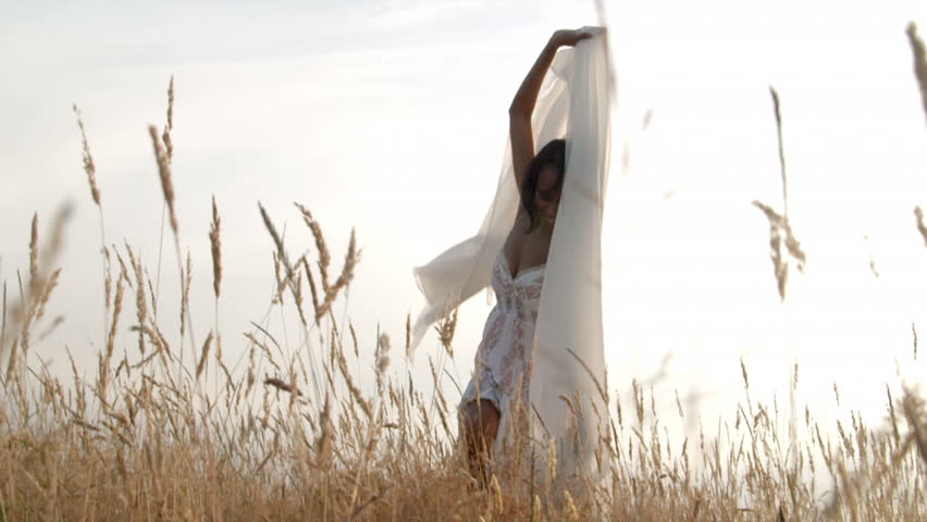 A woman waves a sheer white sheet while moving around a wheat field.