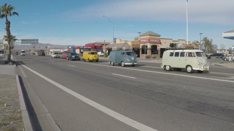 PARKER, AZ/USA - January 22, 2016: Old time camper buses eclipsed by a huge modern recreational vehicle. A giant RV passes by as a line of 1960"s Volkswagen vans roll down the street.