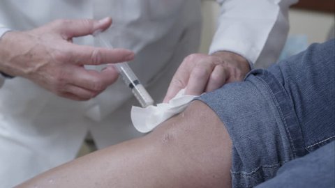 Tight shot of doctor making injection to patient's knee.