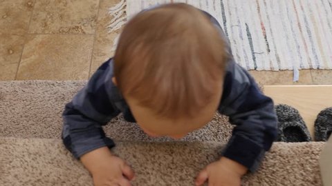 A gimbal shot of a little baby boy learning to crawl up the stairs in his home