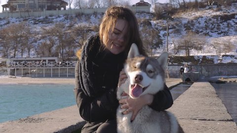 Young woman sitting and palming siberian husky dog on sea pier