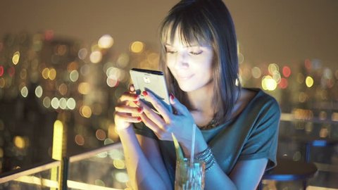 Young, pretty woman using smartphone in bar at night
