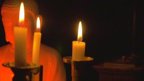 Candlesticks with burning candles in the darkness over a white porcelain statuette of Buddha and a wooden box, dancing music playing on the backgrownd / camera moving forwards - Powered by Shutterstock - Get 15% off with code: PIKWIZARD15